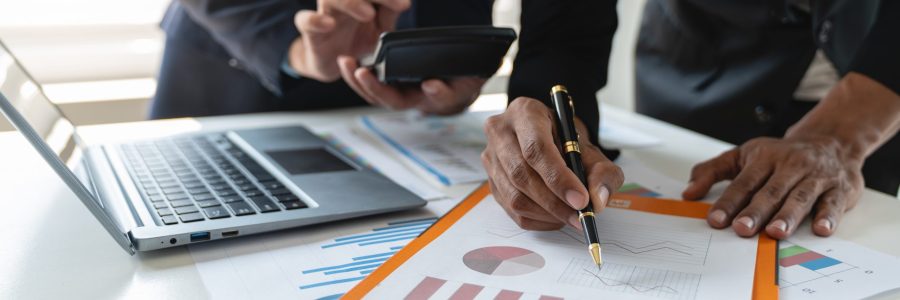 A group of Asian businessmen are brainstorming to analyze financial reporting situations. Calculate investments with income, tax and accounting calculators from graphs data on laptop at desk.
