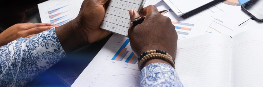 Part of hands of African-Americans in workflow with documents is top view. Various business colleagues sitting at table in modern office working with documents, calculators mobile phone. Can be used as business background